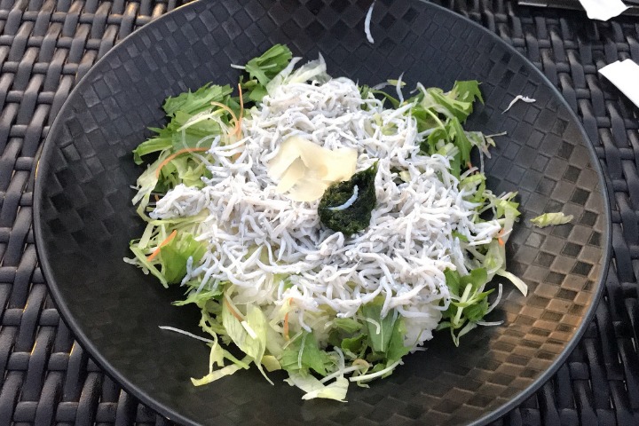 A black bowl of shirasudon topped with fish and salad