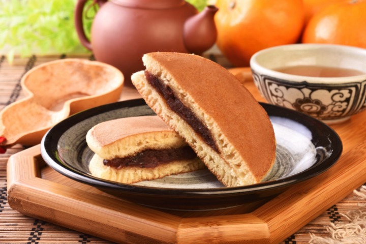 Dorayaki on a black plate with a cup of tea and mandarines