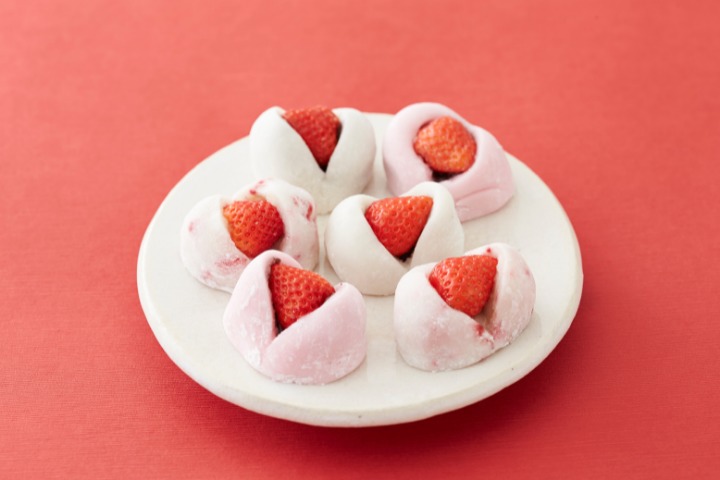 A famous wagashi type called daifuku strawberry mochi on a white plate with red background