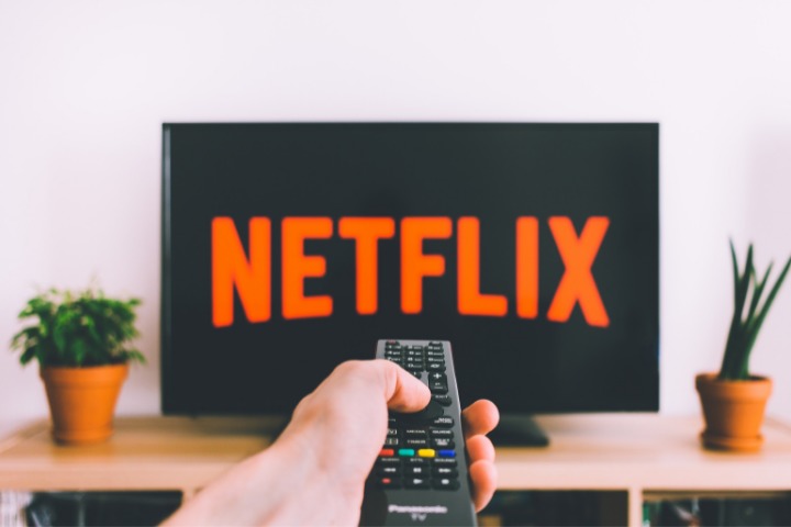 photo of a person with a remote in hand turning on netflix
