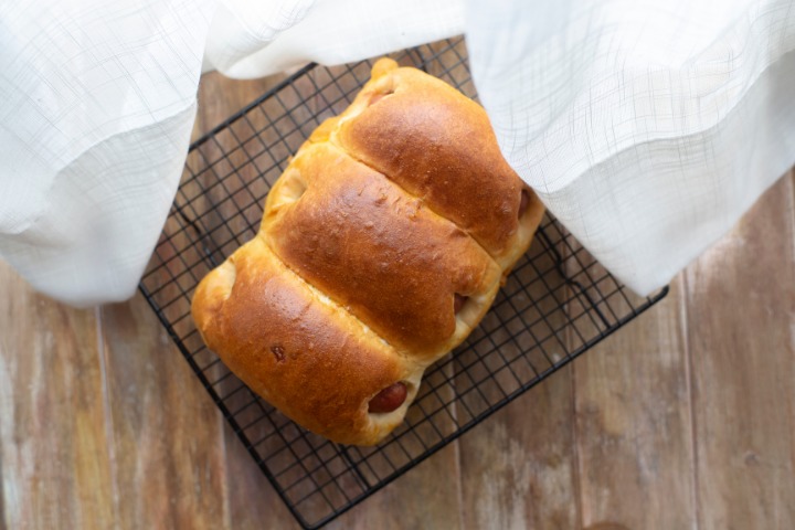 a photo of the japanese wiener hotdog roll bread on a baking tray by some white curtains