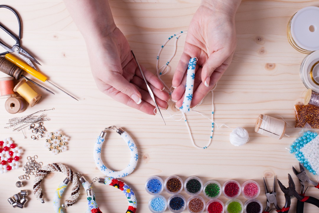 a photo of hands holding equipment for bead accessory making surrounded by tools