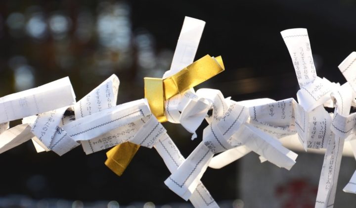 a photo of a golden omikuji among plain omikuji tied to a post