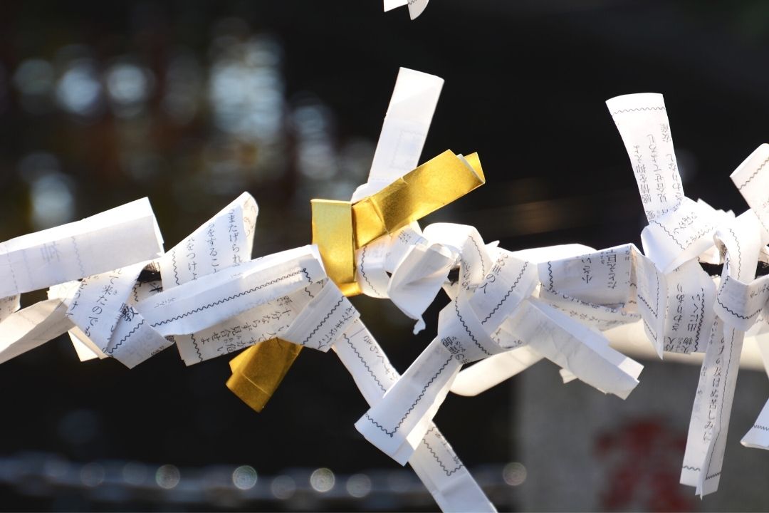 a photo of a golden omikuji among plain omikuji tied to a post