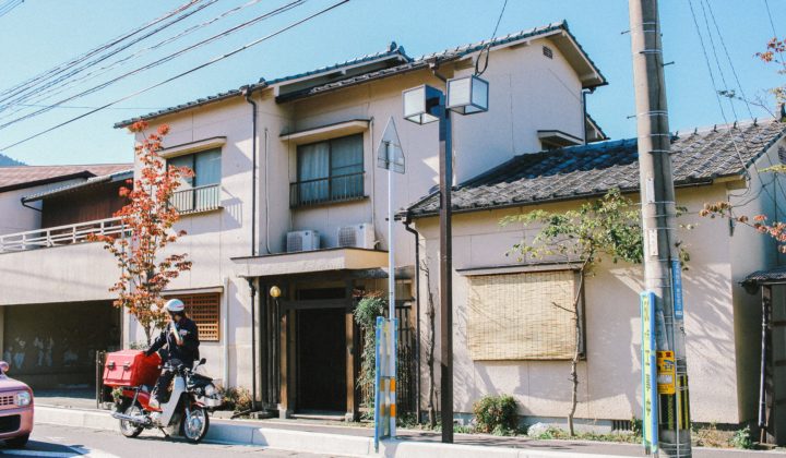 a photo of an abandoned japanese akiya house with a postman in front