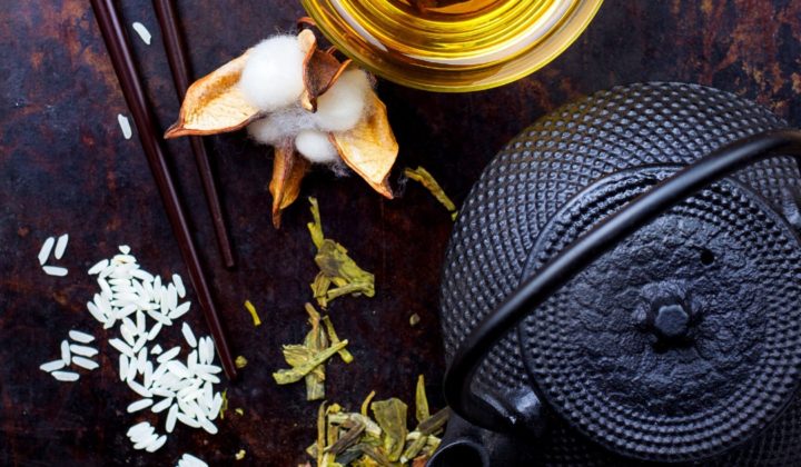 a photo of cotton, an iron teapot, chopsticks, rice, and tea on a dark wood surface
