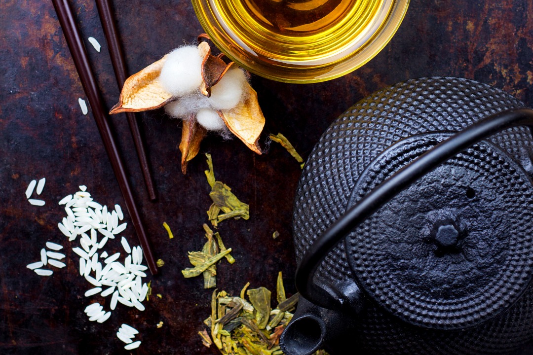 a photo of cotton, an iron teapot, chopsticks, rice, and tea on a dark wood surface