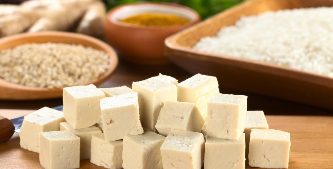 a photo of one of the types of tofu called momen tofu on a wood board with soy beans in background