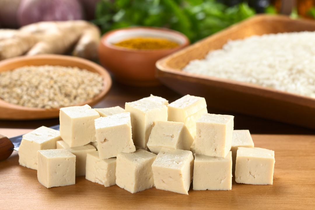 a photo of one of the types of tofu called momen tofu on a wood board with soy beans in background