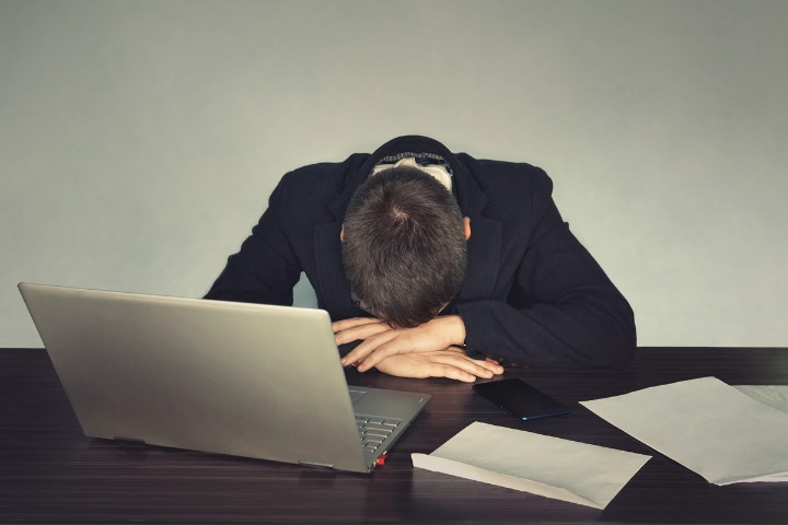 a photo of a man slumped over his laptop tired from overtime