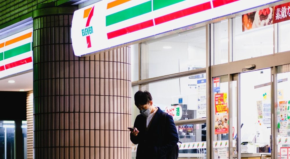 a photo of a man standing out side of a japanese konbini convenience store at night