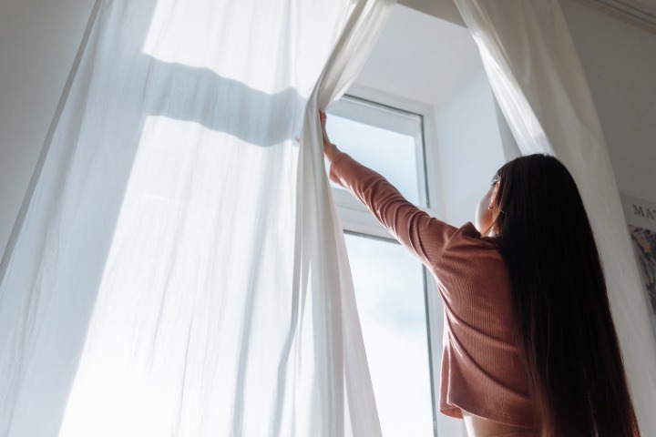 girl opening the curtains on a bright sunny day